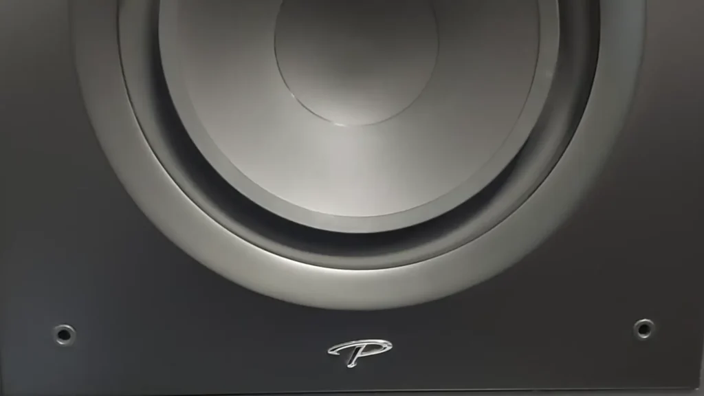 Detailed view of the Paradigm P logo on the bottom corner of the Defiance V12, highlighting the smooth satin finish and the edge of the 12-inch driver.