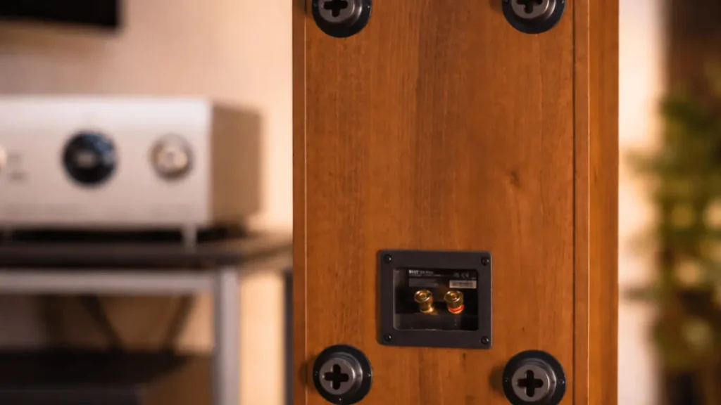 Rear view of the KEF Q4 Meta on-wall speaker in walnut finish, showing gold-plated binding posts and integrated wall-mount points, with Marantz integrated amplifier and Christmas tree in the background.