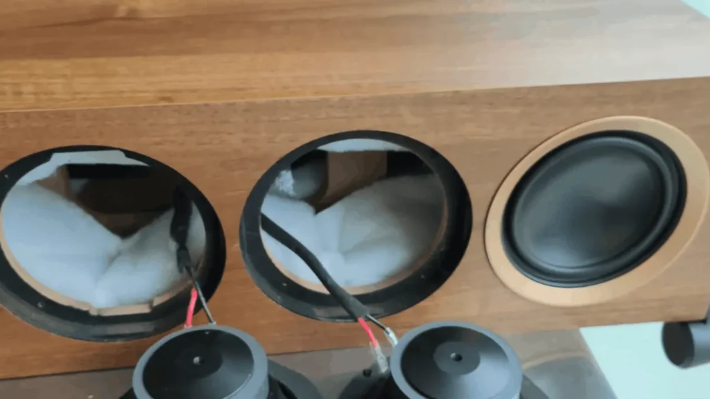 The interior of a MartinLogan F1 cabinet showing white polyfill damping material, internal MDF bracing, and the rear of the aluminum Unibody drivers.