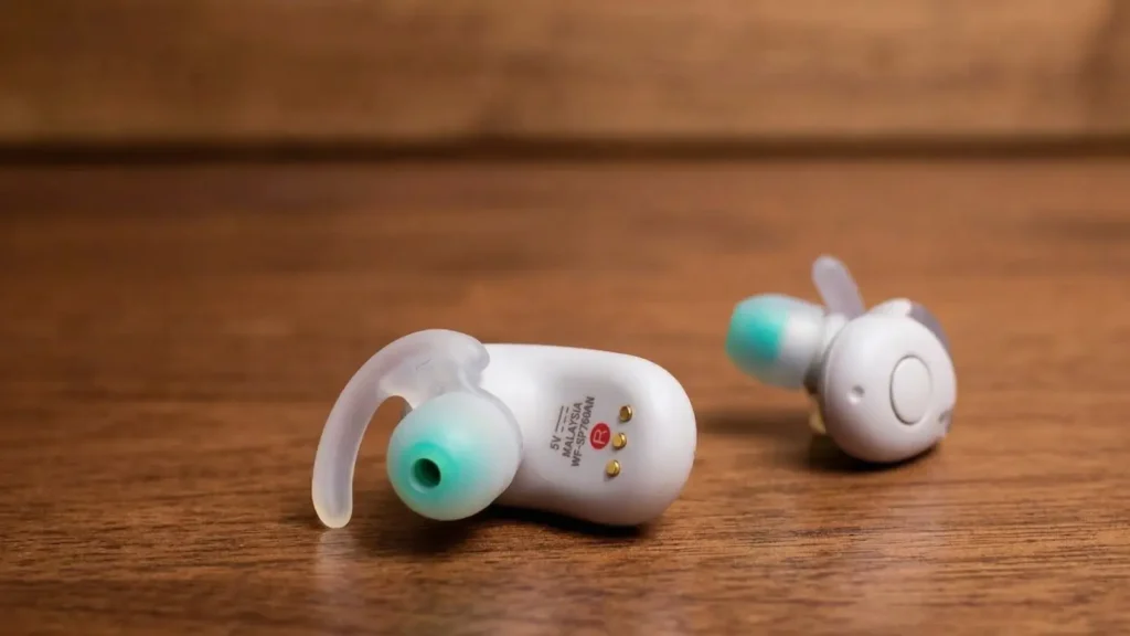 Close-up of the underside of a white Sony WF-SP700N earbud showing the R right-side indicator, charging pins, and Made in Malaysia text