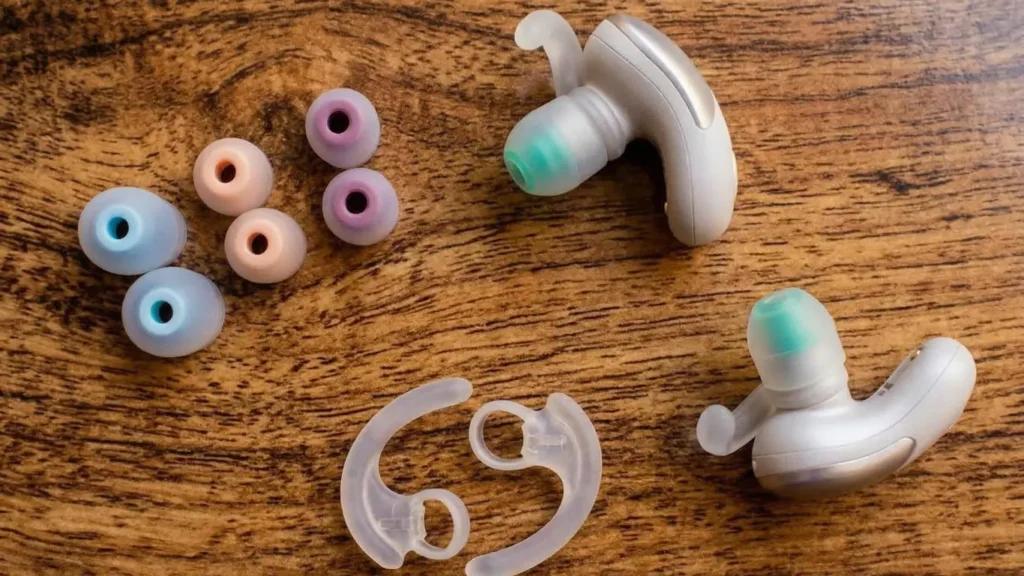 Sony WF-SP700N accessories including three pairs of silicone ear tips in blue, pink, and purple, and two clear silicone wing tips on a wooden surface.